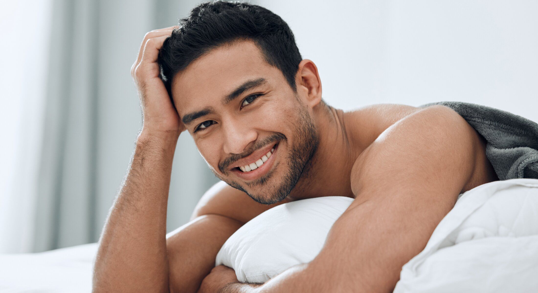 Smiling hair restoration patient model relaxing on bed with pillow.