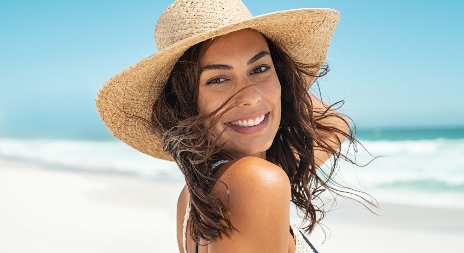 Smiling woman in straw hat at beach.