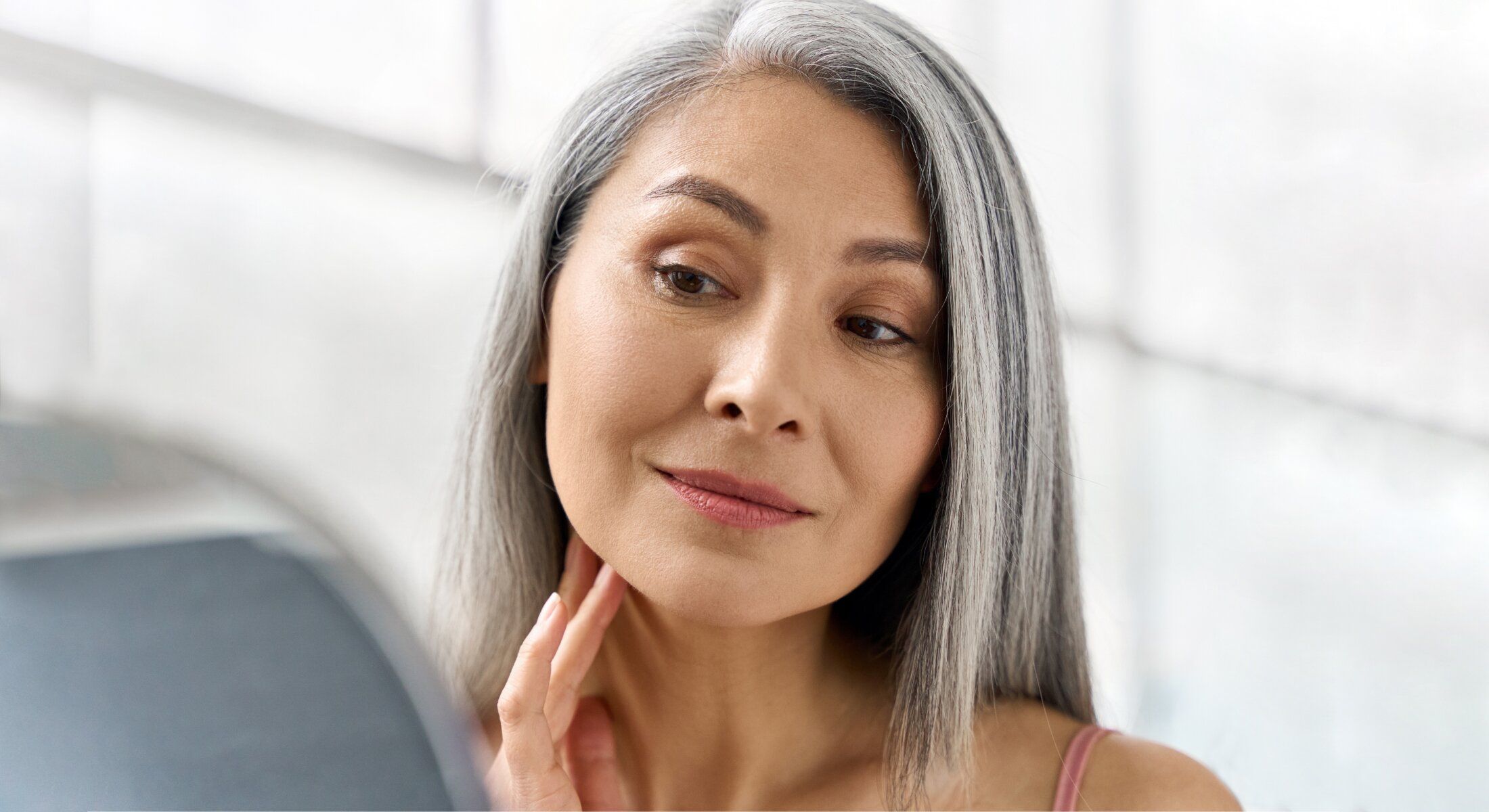 Woman with gray hair examining her reflection.